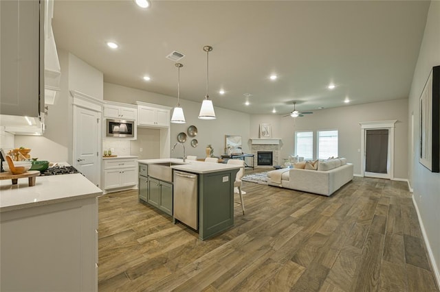 3808 Palmetto Trl, Oklahoma City, OK 73179 - kitchen with built in microwave, ceiling fan, wood finished floors, white cabinets, and a stone fireplace