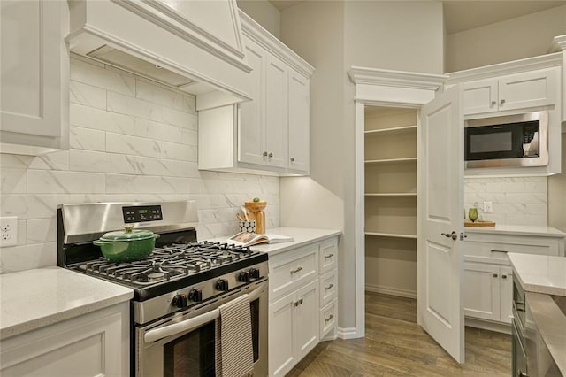 3808 Palmetto Trl, Oklahoma City, OK 73179 - kitchen featuring appliances with stainless steel finishes, backsplash, premium range hood, white cabinets, and wood finished floors
