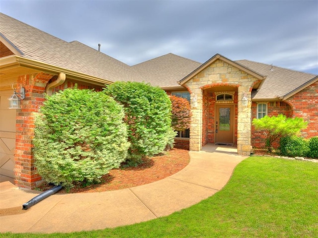 2801 SE 5th St, Moore, OK 73160 - view of exterior entry featuring a shingled roof, stone siding, a yard, and brick siding