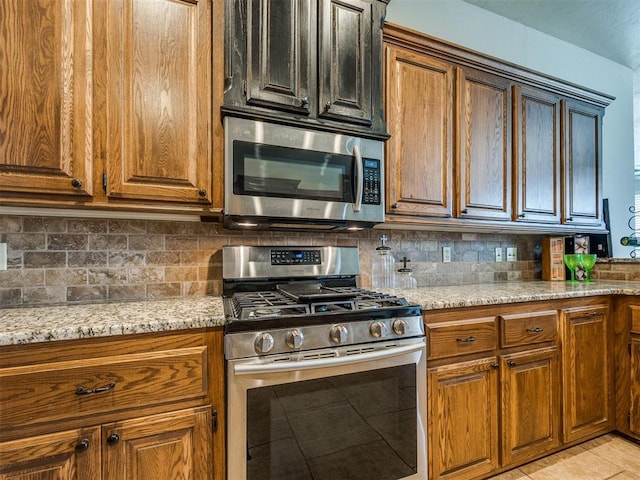 2801 SE 5th St, Moore, OK 73160 - kitchen featuring appliances with stainless steel finishes, backsplash, brown cabinets, and light tile patterned flooring