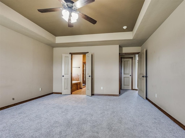 2801 SE 5th St, Moore, OK 73160 - unfurnished bedroom with a tray ceiling, light carpet, connected bathroom, and a ceiling fan