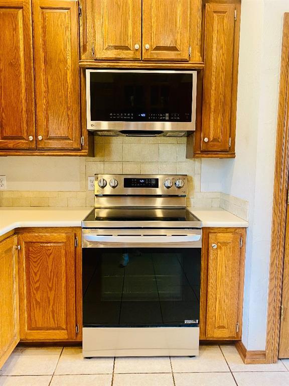 450 Hickory Hill Dr, Choctaw, OK 73020 - kitchen with stainless steel appliances, light countertops, brown cabinets, and decorative backsplash