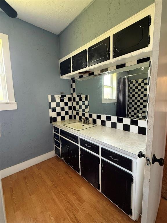 223 N Market St, Cordell, OK 73632 - kitchen with wood finished floors, backsplash, dark cabinetry, light countertops, and a textured ceiling