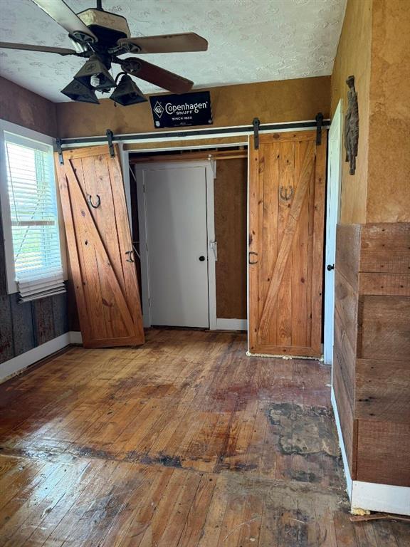 223 N Market St, Cordell, OK 73632 - unfurnished bedroom with a barn door, wood-type flooring, and ceiling fan