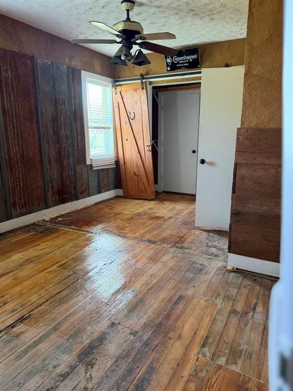 223 N Market St, Cordell, OK 73632 - unfurnished bedroom with hardwood / wood-style flooring, a barn door, a closet, and ceiling fan