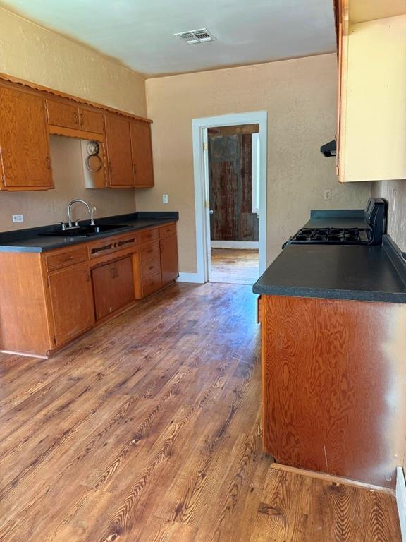 223 N Market St, Cordell, OK 73632 - kitchen with stove, light wood-style flooring, dark countertops, and brown cabinetry