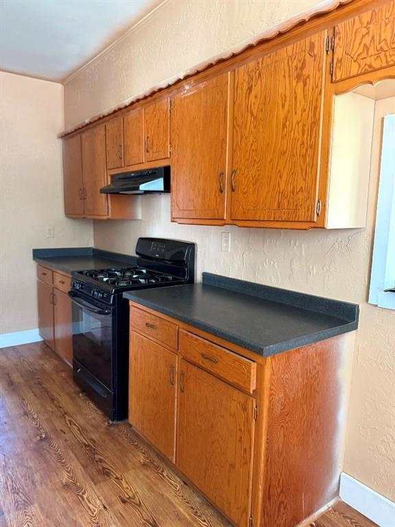 223 N Market St, Cordell, OK 73632 - kitchen featuring black range with gas cooktop, under cabinet range hood, dark wood-type flooring, dark countertops, and brown cabinets