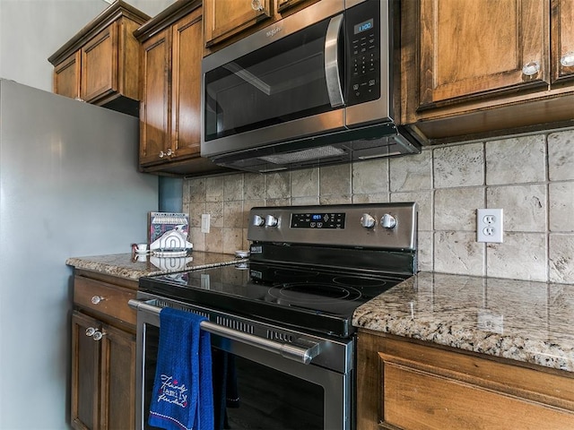 1401 Baycharter St, Norman, OK 73071 - kitchen featuring stainless steel appliances, decorative backsplash, light stone countertops, and brown cabinetry