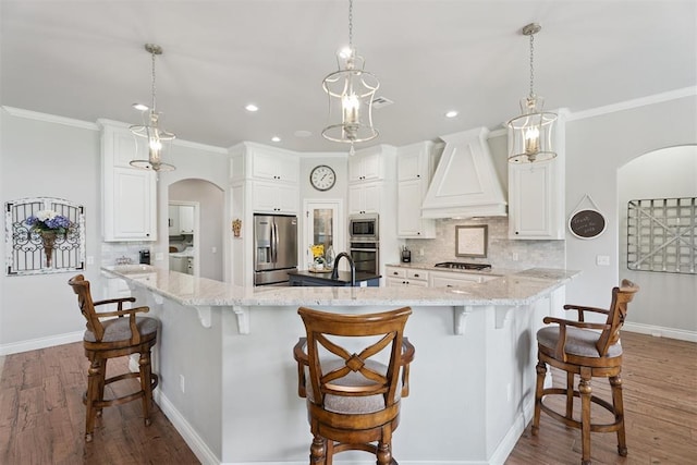 19804 Dalemead Way, Edmond, OK 73012 - kitchen featuring appliances with stainless steel finishes, arched walkways, premium range hood, a large island with sink, and backsplash