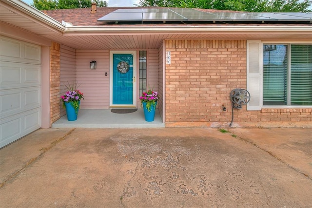 100 Three Oaks Dr, Midwest City, OK 73130 - entrance to property featuring brick siding, roof mounted solar panels, an attached garage, roof with shingles, and a porch