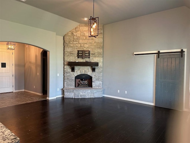 5024 SW 130th St, Oklahoma City, OK 73173 - unfurnished living room featuring lofted ceiling, arched walkways, wood finished floors, a barn door, and a fireplace