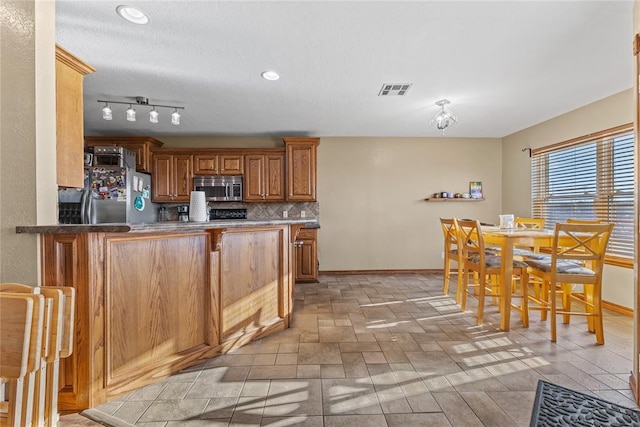 3008 Fairway Dr, Weatherford, OK 73096 - kitchen featuring stainless steel appliances, backsplash, a peninsula, brown cabinetry, and recessed lighting