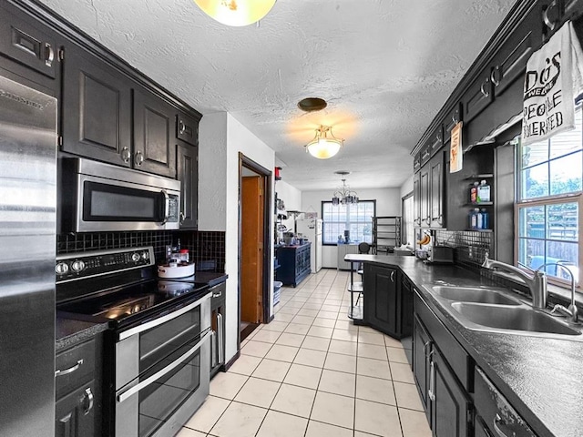 521 E Broadway St, Lexington, OK 73051 - kitchen with stainless steel appliances, light tile patterned flooring, decorative backsplash, dark cabinetry, and a chandelier