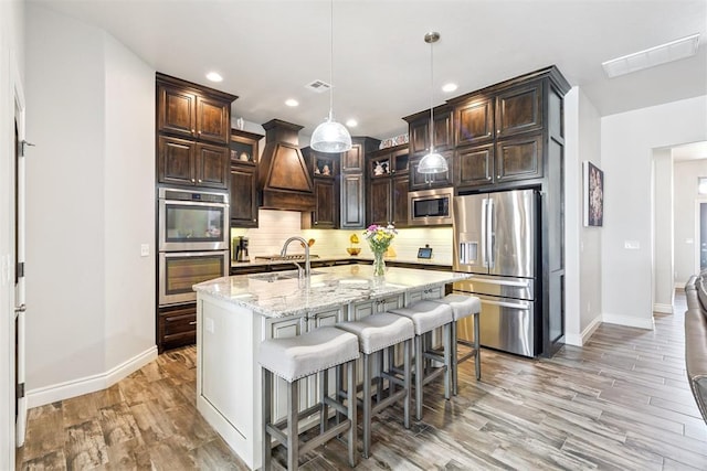 12505 Shady Gln, Choctaw, OK 73020 - kitchen featuring appliances with stainless steel finishes, premium range hood, tasteful backsplash, light wood finished floors, and dark brown cabinetry