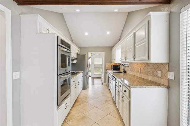 2416 Chimney Hill Ct, Edmond, OK 73034 - kitchen with stainless steel appliances, white cabinetry, vaulted ceiling, backsplash, and light tile patterned flooring