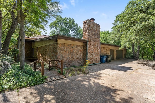 4225 Red Bud Pl, Edmond, OK 73013 - view of property exterior with stone siding, a chimney, driveway, and a garage