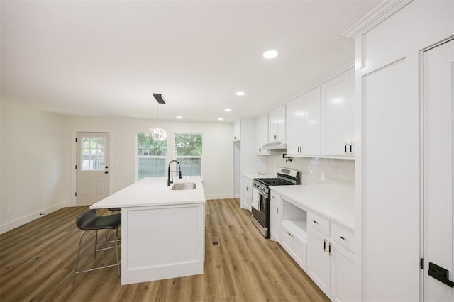2020 Hasley Dr, The Village, OK 73120 - kitchen with stainless steel gas stove, white cabinetry, under cabinet range hood, light wood-style flooring, and light countertops