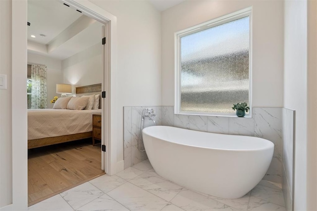 200 Pont Neuf Ct, Edmond, OK 73034 - ensuite bathroom featuring marble look tiles, a freestanding tub, tile walls, plenty of natural light, and a wainscoted wall