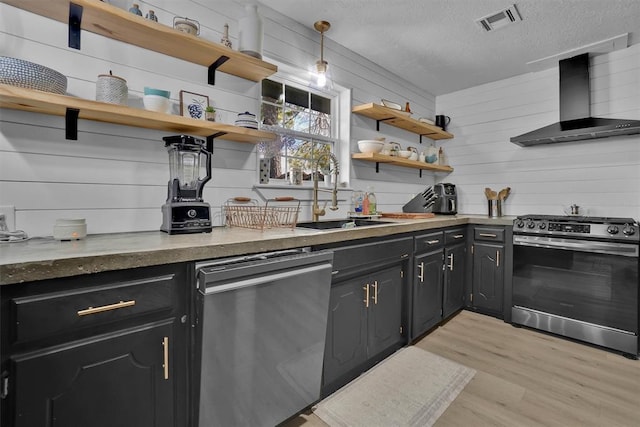 323 W 13th St, Snyder, OK 73566 - kitchen featuring appliances with stainless steel finishes, wall chimney range hood, open shelves, light wood-type flooring, and a textured ceiling