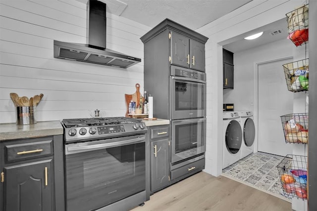 323 W 13th St, Snyder, OK 73566 - kitchen featuring stainless steel appliances, wall chimney range hood, washing machine and dryer, light wood-type flooring, and wood walls
