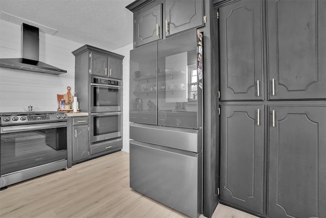 323 W 13th St, Snyder, OK 73566 - kitchen with stainless steel appliances, wall chimney exhaust hood, light wood finished floors, a textured ceiling, and gray cabinetry