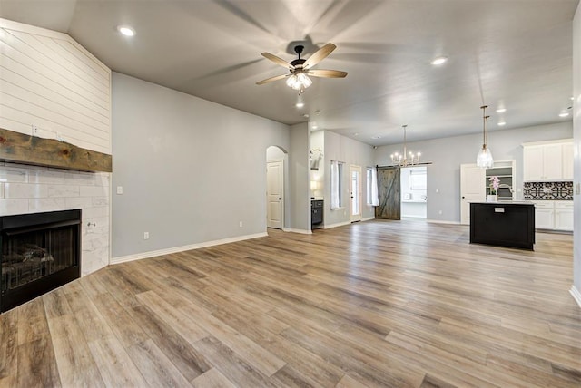 9021 NW 74th St, Yukon, OK 73099 - unfurnished living room featuring a ceiling fan, a tile fireplace, arched walkways, light wood finished floors, and recessed lighting