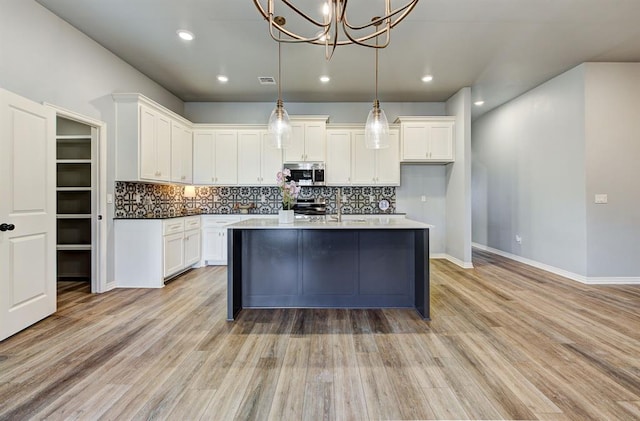 9021 NW 74th St, Yukon, OK 73099 - kitchen with stainless steel appliances, white cabinets, a chandelier, backsplash, and light wood finished floors