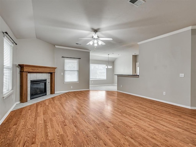 10808 Cheshire Ct, Yukon, OK 73099 - unfurnished living room featuring a tiled fireplace, a ceiling fan, light wood-style floors, a chandelier, and crown molding