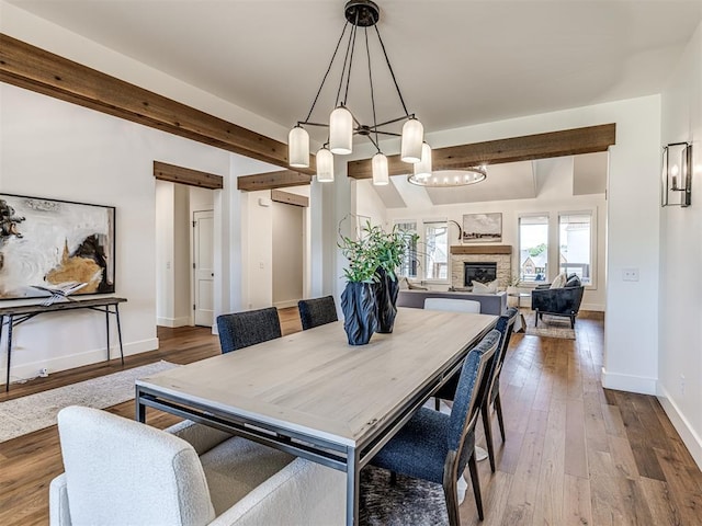 7308 Sunset Sail Ave, Edmond, OK 73034 - dining space featuring a chandelier, beamed ceiling, a stone fireplace, and wood finished floors