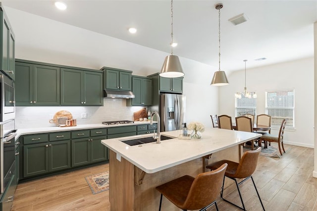 15921 Bison Dr, Moore, OK 73170 - kitchen with green cabinets, appliances with stainless steel finishes, under cabinet range hood, decorative backsplash, and light wood-style flooring
