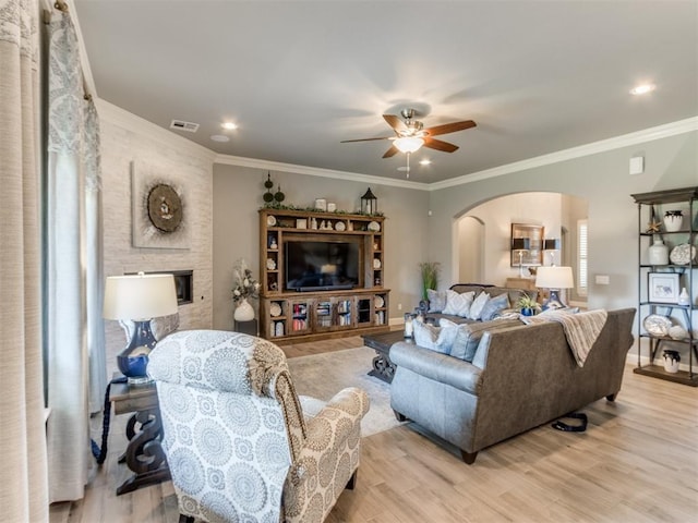 13308 NW 6th St, Yukon, OK 73099 - living room featuring arched walkways, a ceiling fan, light wood-style floors, crown molding, and a fireplace