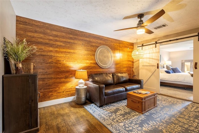 19277 E 1220th Rd, Sayre, OK 73662 - living area featuring a barn door, a ceiling fan, wood finished floors, a textured ceiling, and wooden walls