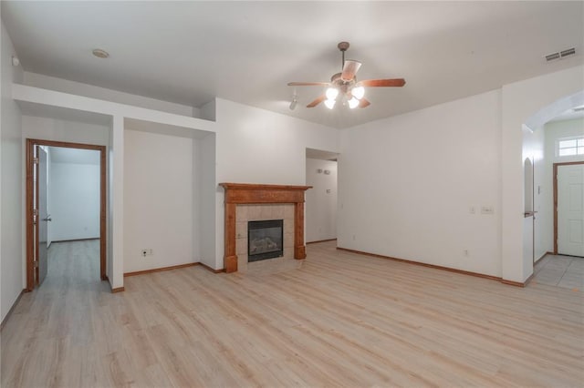 2412 NW 164th Ter, Edmond, OK 73013 - unfurnished living room featuring arched walkways, light wood-style flooring, ceiling fan, and a tile fireplace