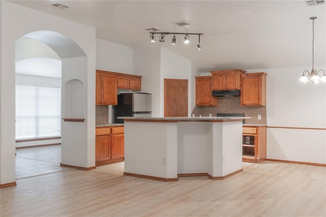 2412 NW 164th Ter, Edmond, OK 73013 - kitchen with freestanding refrigerator, under cabinet range hood, brown cabinetry, light wood finished floors, and vaulted ceiling