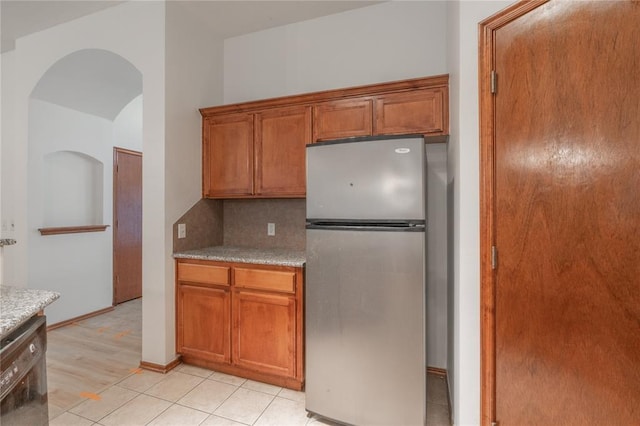 2412 NW 164th Ter, Edmond, OK 73013 - kitchen with freestanding refrigerator, brown cabinets, backsplash, arched walkways, and light tile patterned flooring