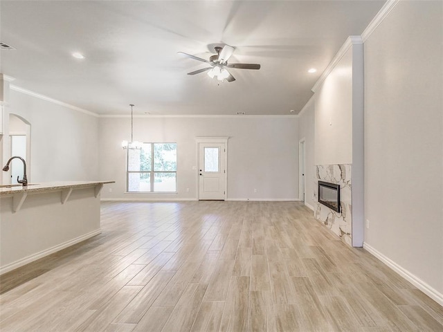 9070 Oak Tree Cir, Edmond, OK 73025 - unfurnished living room with a ceiling fan, a high end fireplace, ornamental molding, light wood-type flooring, and arched walkways