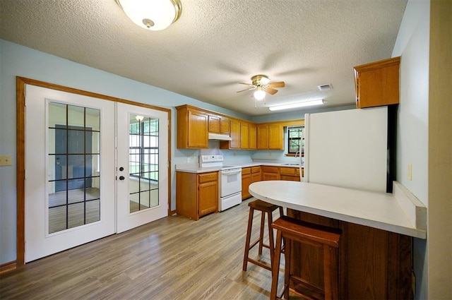 1001 Norris Ave, Broken Bow, OK 74728 - kitchen with white appliances, a peninsula, light wood-style flooring, french doors, and under cabinet range hood