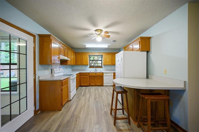 1001 Norris Ave, Broken Bow, OK 74728 - kitchen featuring white appliances, under cabinet range hood, a peninsula, light wood-type flooring, and a textured ceiling