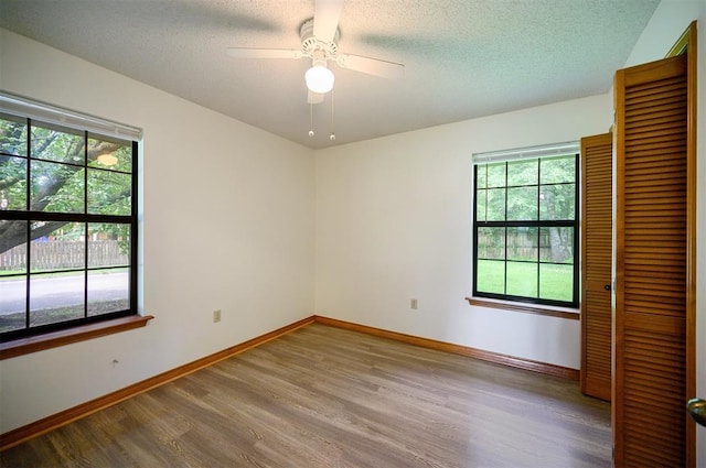 1001 Norris Ave, Broken Bow, OK 74728 - unfurnished bedroom featuring wood finished floors, multiple windows, a closet, a textured ceiling, and ceiling fan