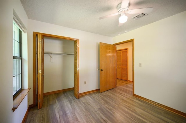 1001 Norris Ave, Broken Bow, OK 74728 - unfurnished bedroom with wood finished floors, multiple windows, a closet, a textured ceiling, and a ceiling fan