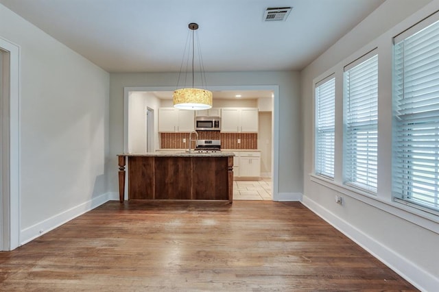 2524 NW 15th St, Oklahoma City, OK 73107 - kitchen featuring stainless steel appliances, backsplash, white cabinetry, light wood finished floors, and pendant lighting