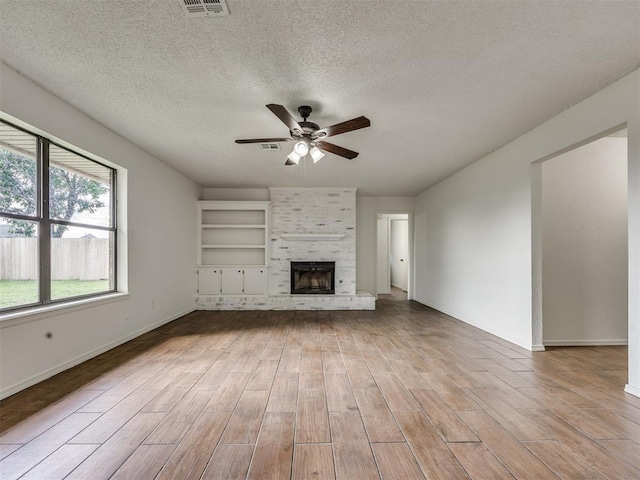 8317 Curtis Ter, Oklahoma City, OK 73132 - unfurnished living room featuring a ceiling fan, light wood-style flooring, a brick fireplace, and a textured ceiling