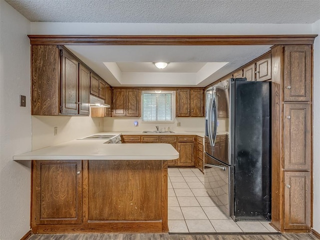 10428 Fairfax Ln, Yukon, OK 73099 - kitchen featuring freestanding refrigerator, a peninsula, under cabinet range hood, light countertops, and a textured ceiling