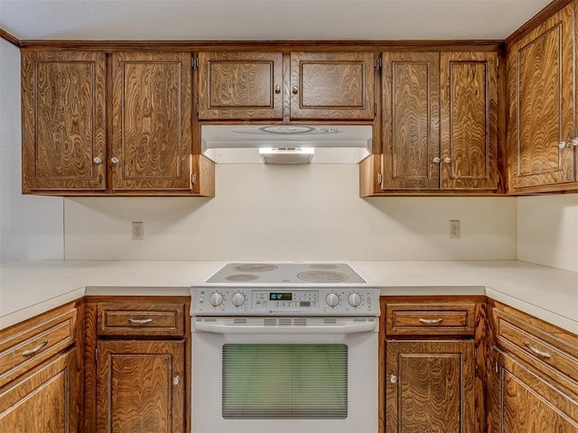 10428 Fairfax Ln, Yukon, OK 73099 - kitchen featuring white range with electric stovetop, range hood, light countertops, and brown cabinets