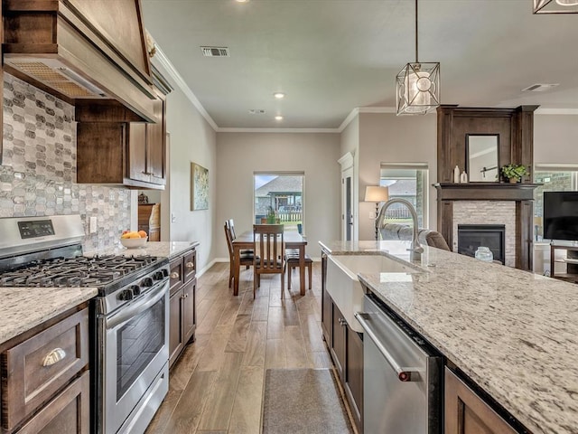 18716 Lazy Grove Dr, Edmond, OK 73012 - kitchen with stainless steel appliances, custom exhaust hood, a fireplace, decorative backsplash, and light wood-type flooring