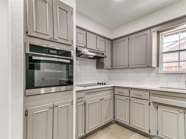 502 Walnut Ave, Yukon, OK 73099 - kitchen with gray cabinets, under cabinet range hood, stainless steel oven, black electric cooktop, and tasteful backsplash