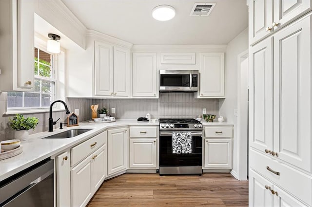 908 NW 12th St, Moore, OK 73160 - kitchen with appliances with stainless steel finishes, backsplash, white cabinetry, light countertops, and light wood-type flooring