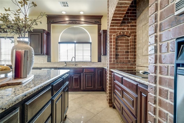 1704 NW 171st St, Edmond, OK 73012 - kitchen featuring black electric stovetop, light tile patterned flooring, light stone countertops, and brick wall