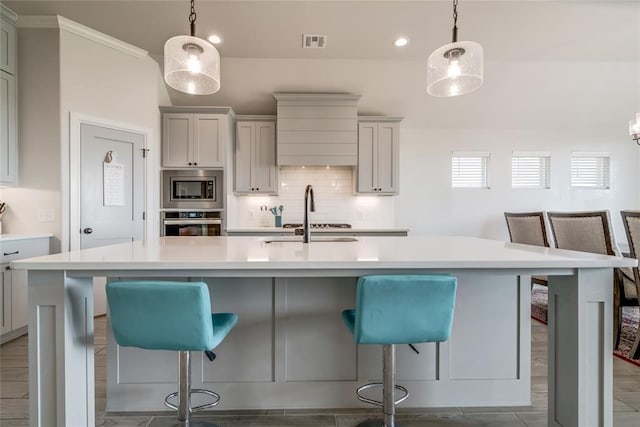 18445 Austin Pl, Edmond, OK 73012 - kitchen featuring appliances with stainless steel finishes, backsplash, light countertops, a kitchen breakfast bar, and an island with sink