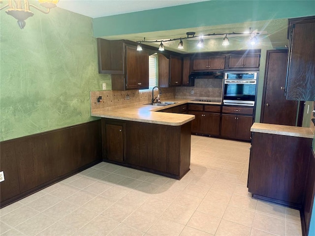 2608 SW 93rd, Oklahoma City, OK 73159 - kitchen with stainless steel oven, a peninsula, dark brown cabinetry, light countertops, and a wainscoted wall